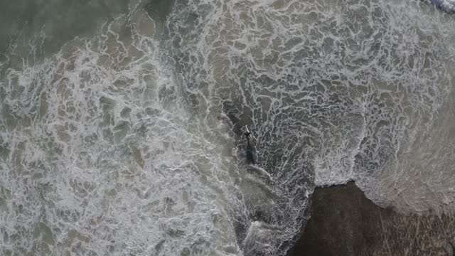 The waves crash into the sea and the surfer gets ready