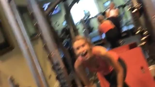 Girl in a pink top at a gym falls after lifting heavy weight