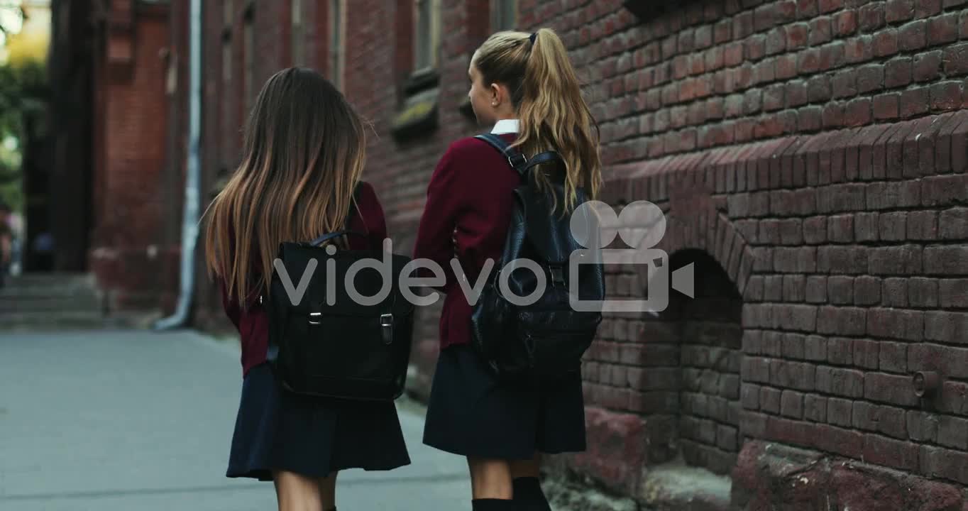 Two Teen Girls In The Uniforms Coming Back From School Home And Walking The Street While Talking