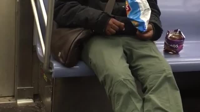 Guy is sleeping and also eats bags of doritos and lays chips on subway train