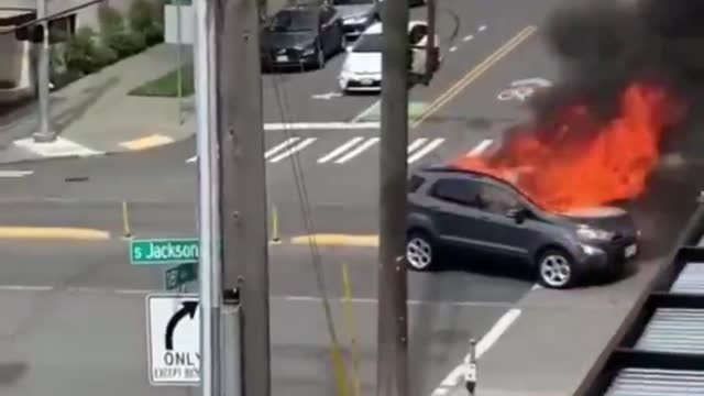 THE CURRENT STATE OF SEATTLE: Car in flames while man exposes himself peeing on the sidewalk.