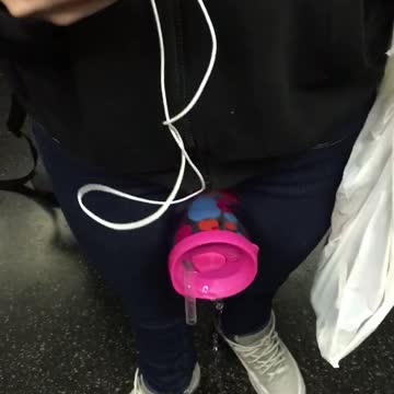 Pink cup between legs spilling onto subway floor