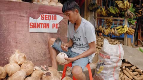 Tracking Shot of Young Man Shaving Coconut Coir Fibre