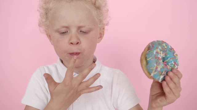 Cute Little Boy Licking Fingers with Donut in Hand