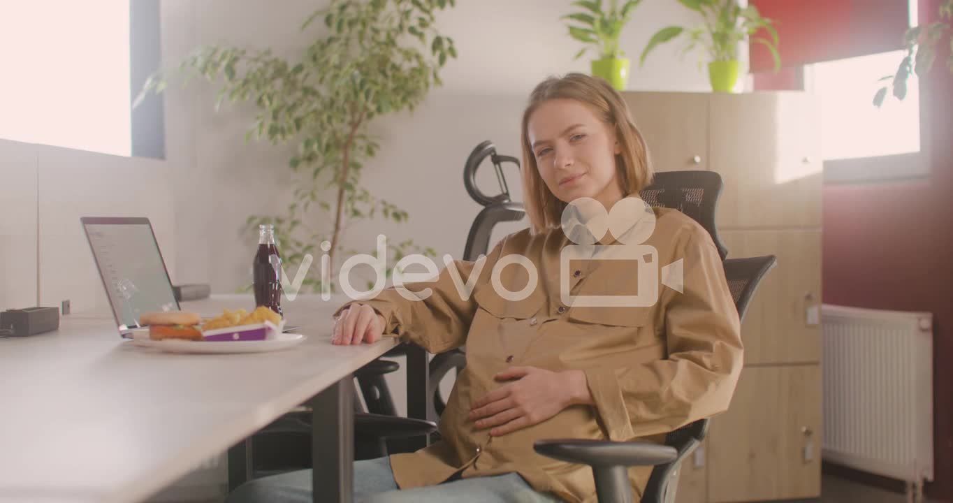 Working Pregnant Woman Sitting At Desk And Smiling At Camera During Office Lunch Break