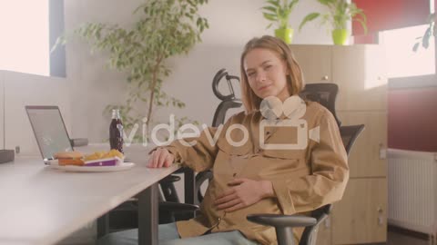 Working Pregnant Woman Sitting At Desk And Smiling At Camera During Office Lunch Break