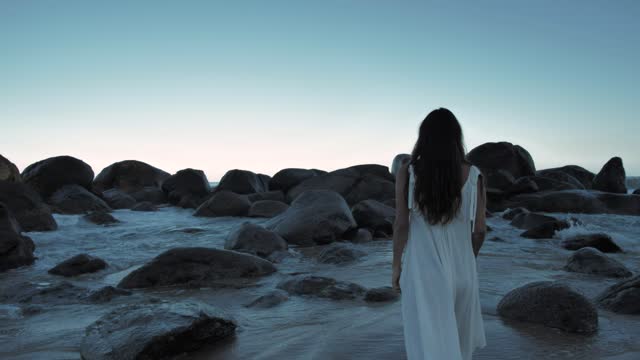 Woman walking on beach towards boulders