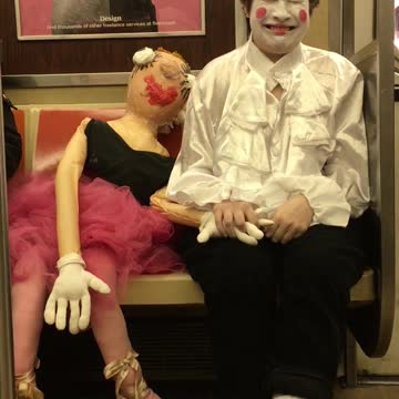 Girl dressed as a mime holds hands with a mannequin doll on subway train