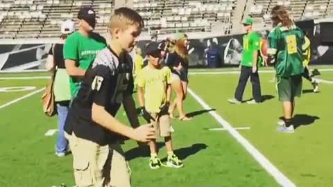 Boy in black jersey kicks ball hits girl in green