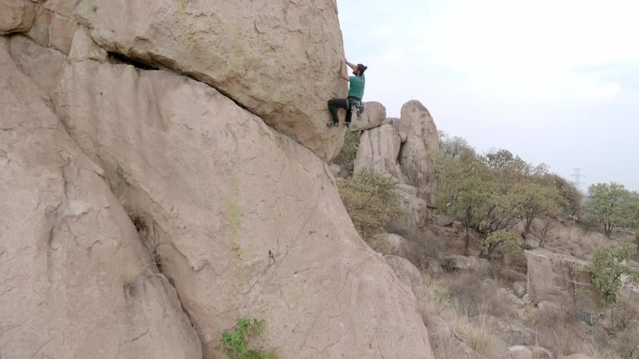 Alpinist climbing a huge rock in a desert