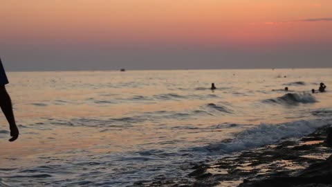 Man walking along the shore of a beach at sunset