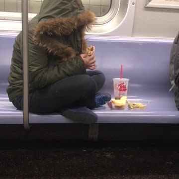 Woman sits criss-cross on subway seat and eats sandwich