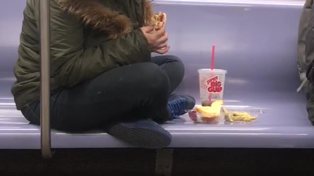 Woman sits criss-cross on subway seat and eats sandwich