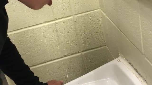 Guy in black shirt throwing up on sink in restroom