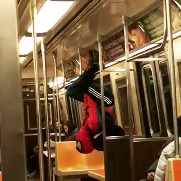 Man in spiderman outfit hangs from subway ceiling