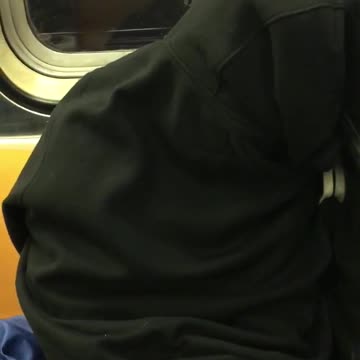 Person fully covered in black jacket on subway sleeping