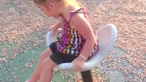 Little girl on white spinning chair at park spins too much and falls off