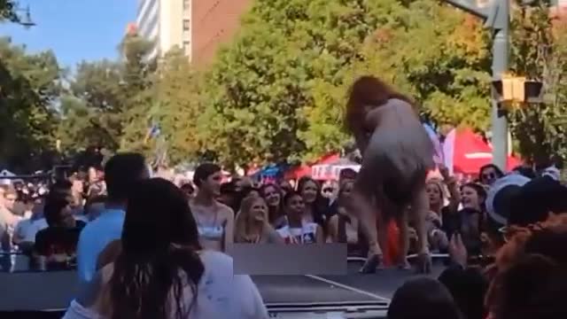 A drag queen teaches a young child to perform and collect cash tips at a pride event