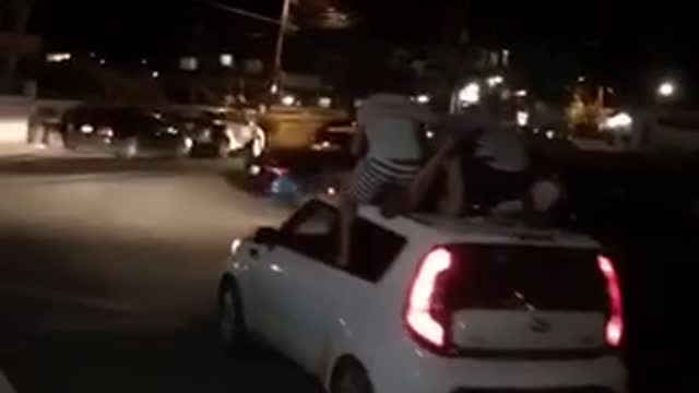 Night time three guys on top of kia soul car paddling while car is moving driving