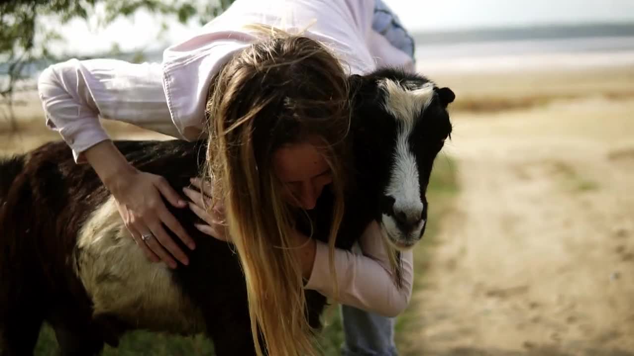 Woman stroking goat outdoors, caresses it with both hands