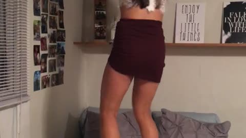 Woman in white shirt and black skirt is jumping on bed and accidentally jumps into fan