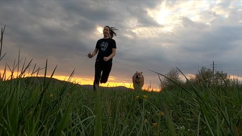 Lady Running With Her Dog In A Grass Field