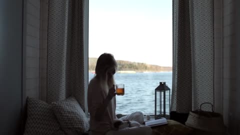 girl with a puppy reading a book and drinking tea sitting by the window with a lake view