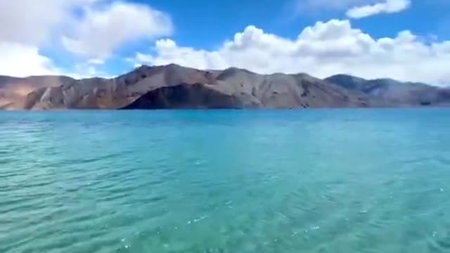 Clear Blue Water of Famous Lake Washes Shore Against Beautiful Mountains