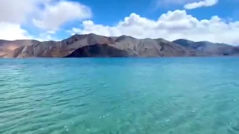 Clear Blue Water of Famous Lake Washes Shore Against Beautiful Mountains