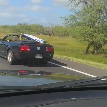Guy in black car holding surfboard over his head