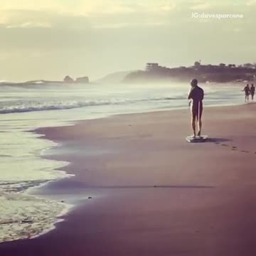 Man in black dragging surfboard on beach