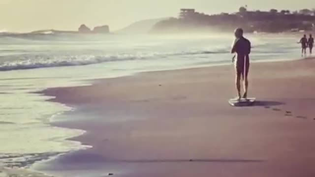 Man in black dragging surfboard on beach
