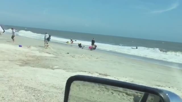 Couple eating in car watch two people attempt to use raft in ocean