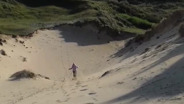 Blue shirt lady running down sand dune hill faceplants