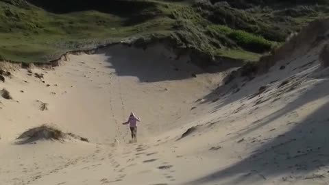 Blue shirt lady running down sand dune hill faceplants