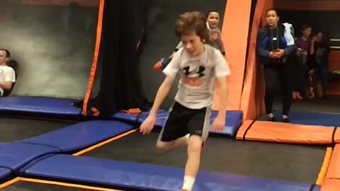 Boy in grey shirt does flip on orange trampoline, falls on head