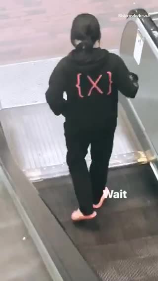 Man x on black sweater walking opposite escalator