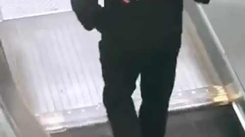 Man x on black sweater walking opposite escalator