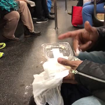 Guy in black jacket eating food with fingers on subway