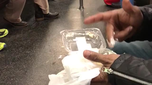 Guy in black jacket eating food with fingers on subway