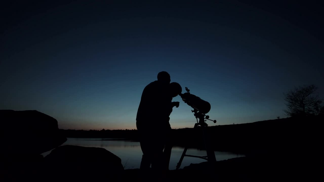 Man and a boy you using the telescope at dusk