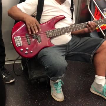 Man hanging from subway plays red guitar