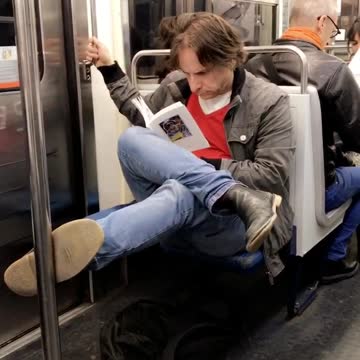 Cross legged man on subway reads book