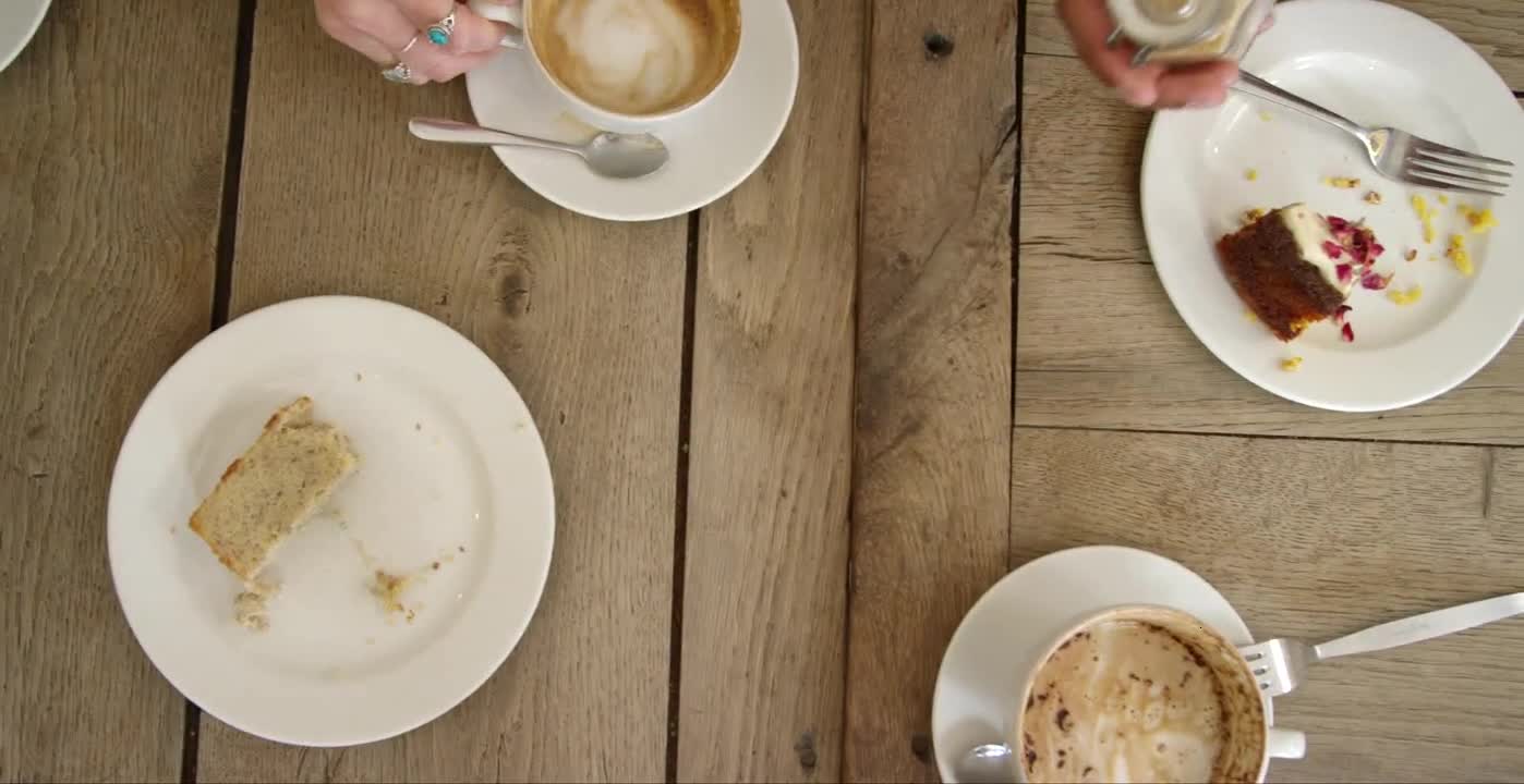 Overhead View Of Hands Lifting Cups Of Coffee And Cake Off Cafe Table