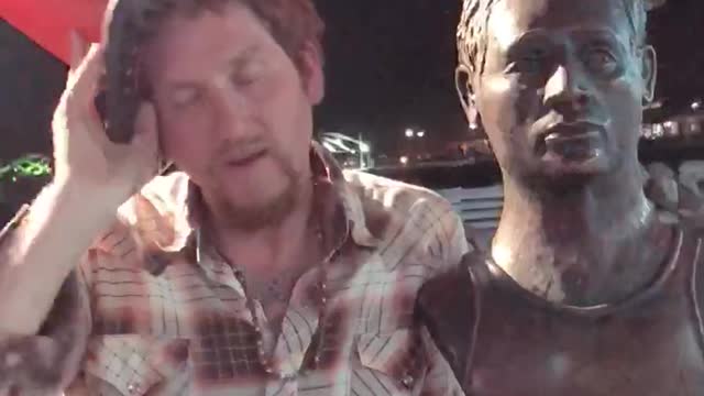 Drunk man next to statue orange cones on heads
