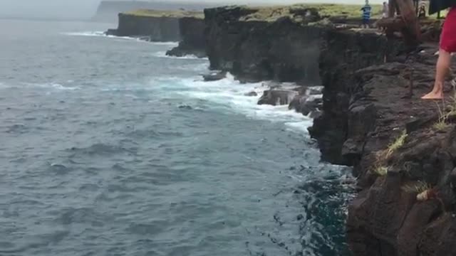 Shirtless man backflipping off ladder on cliff flops