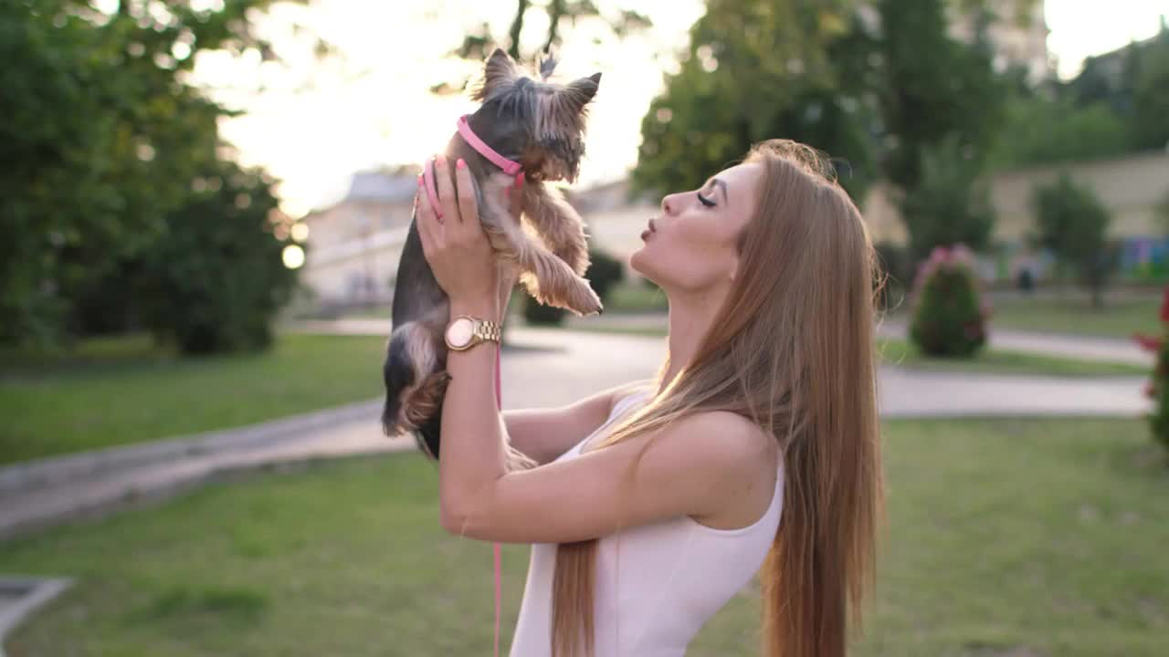 Beautiful Girl Walking With Her Small Dog In The City Park And Using Smartphone