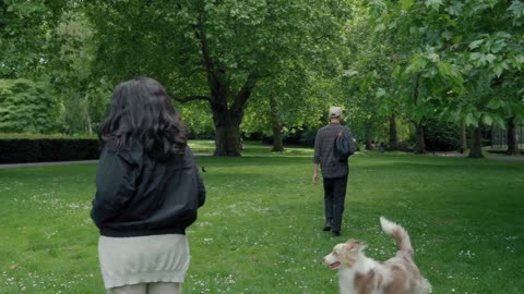 A couple is walking with an Australian shepherd in the park