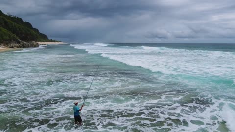 Drone Footage of a Man Fishing in Shallow Water on a Beach