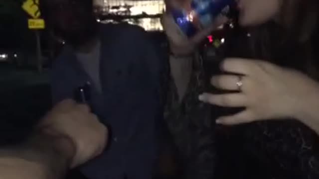 Girl in brown dress chugs half beer in parking lot